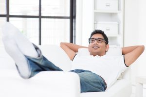 Indian guy daydreaming and rest at home. Asian man relaxed and lying on sofa indoor. Handsome male model.